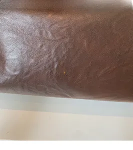 Macro shot of brown leather tote bag with lychee texture and gold-stamped brand logo