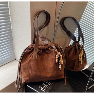 Close-up of brown suede bucket bag with wooden bead charm and smooth leather handle