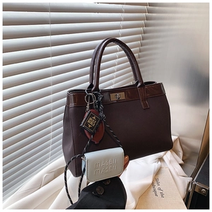 Detailed close-up of a brown tote bag featuring a metal twist lock and unique charms