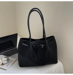 Detail of black woven texture tote bag with metal buckle next to a laptop and book