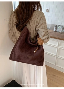 Detail of large brown suede shoulder bag with tassel and plush ball charms on a model