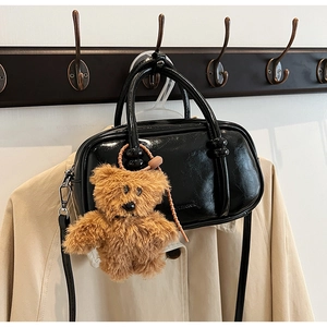 Glossy black bowling bag detail with plush bear charm hanging on a vintage wooden coat rack