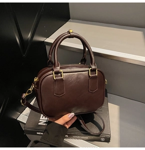 Detail view of a chocolate brown mini Boston bag with shiny leather and gold hardware