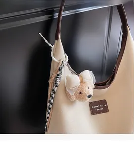 Gros plan d'un charm ours en peluche avec nœud en dentelle sur un sac à bandoulière en toile