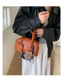 Detail view of brown leather handbag with zipper pocket and cute bear plush charm