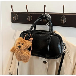 Detail of a black glossy doctor bag with teddy bear charm on a wooden coat rack