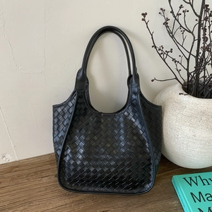 Detail of black woven leather tote bag with sturdy straps on a rustic wooden table