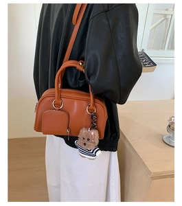 Chic brown Boston bag with teddy bear pendant and crossbody strap shown on model