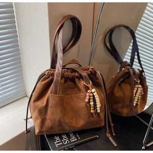 Detail of dark brown suede bucket bag featuring drawstring and decorative wooden beads