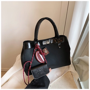 Detail of matte black handbag featuring glossy patent handles and a silver metal clasp