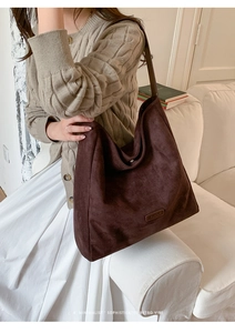 Detail of dark brown suede tote bag featuring a brand plaque and soft textured finish