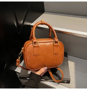 Close-up of brown vintage Boston bag with gold hardware held over classic books