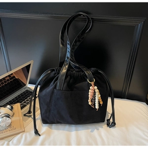 Detail of black drawstring bucket bag with beaded charm in a modern office setup
