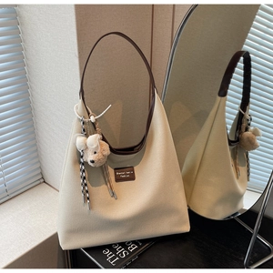 Détail du sac fourre-tout en toile beige avec anses en cuir brun et pendentif ours