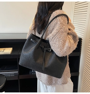 Detail of black woven tote bag featuring adjustable side straps and metallic buckle