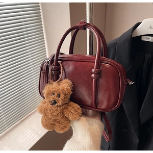 Detail view of burgundy leather bowling bag with plush bear charm and crossbody strap