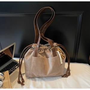 Detail view of tan faux suede bucket bag with wooden bead charm and side pockets