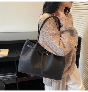 Side view of a black woven tote bag worn by a model in a minimalist setting