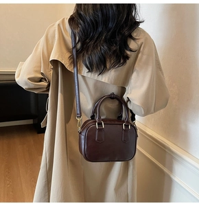 Rear view of model wearing a vintage dark brown leather crossbody bag with beige trench coat