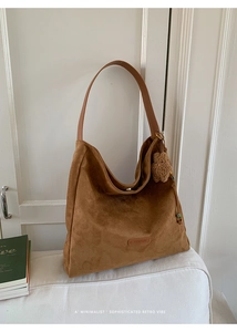 Detail of a brown suede hobo bag with leather strap and a plush bear pendant