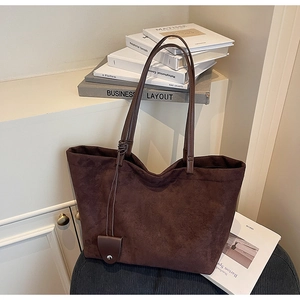 Detail view of large dark brown suede tote bag featuring slim straps and a metal buckle charm