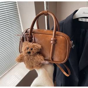 Close-up of vintage brown bowling bag with plush teddy bear charm on a clothes rack