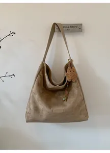 Macro shot of khaki suede tote bag detail featuring brand logo and plush bear charm