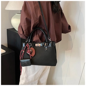 Close-up of black matte satchel with silver lock, red charm and mini purse detail