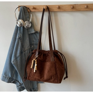 Detail of dark brown faux suede tote bag with drawstring closure and wooden bead charm