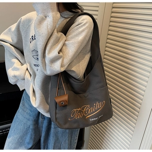 Detail of dark grey canvas tote bag with orange embroidery and brown leather charm