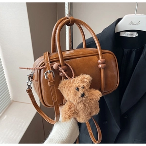 Detailed macro view of brown PU leather texture and plush bear charm on the bag