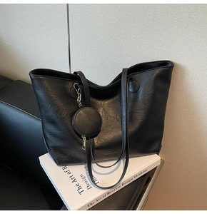 Detail of classic black tote bag with small round coin purse on a leather sofa