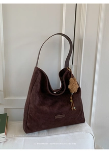 Detail of dark brown tote bag with suede texture, PANTOR logo plate and plush bear charm