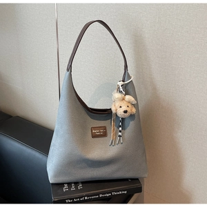 Détail du sac cabas en toile grise avec garniture en cuir brun et breloque chiot