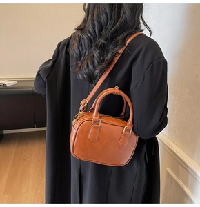 Close-up of caramel leather crossbody bag with gold hardware on black blazer model