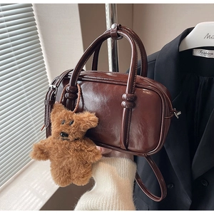 Detailed view of glossy dark brown retro handbag with plush bear charm and dual handles