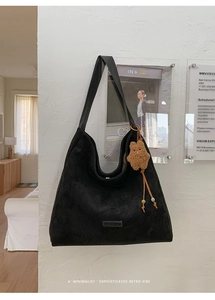 Detail of minimalist black suede hobo bag with metal logo and cute brown bear pendant
