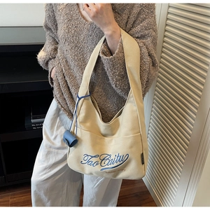 Detailed close-up of beige canvas tote bag with blue embroidery and mini pouch accessory