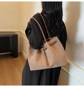 Model wearing a large khaki woven tote bag with brown leather straps and side buckle