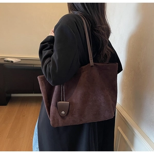 Lifestyle view of dark brown suede tote bag carried by model in minimalist room
