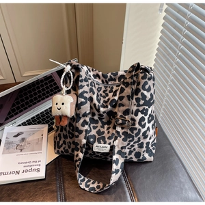 Detail of leopard canvas tote bag with bread plush charm on a leather seat