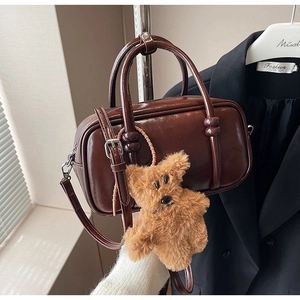Detail view of dark brown patent leather bowling bag with cute plush bear charm