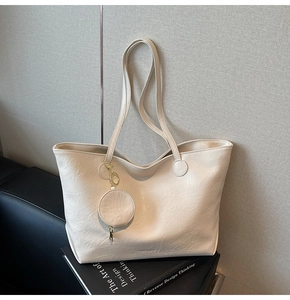 Detail of a creamy off-white tote bag with pleated texture and small round purse charm