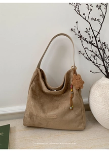 Detail of tan suede tote bag with brand logo and cute brown teddy bear keychain