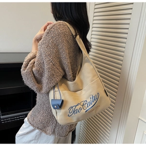 Detail of beige canvas tote bag featuring blue embroidery and matching mini pouch accessory