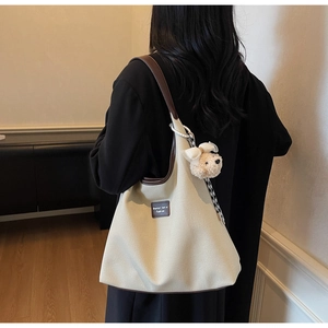 Détail du sac à bandoulière en toile beige avec garniture en cuir brun et breloque chien