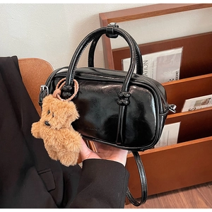 Detail of a glossy black mini bowling bag featuring a cute brown plush bear charm