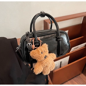 Glossy black bowling bag with brown plush bear charm and knotted handles detail