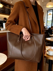 Detail of dark brown tote bag on wool coat showing its large capacity and matte leather texture