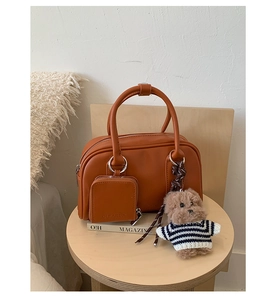 Brown leather handbag detail with small pouch and cute plush bear charm on a table